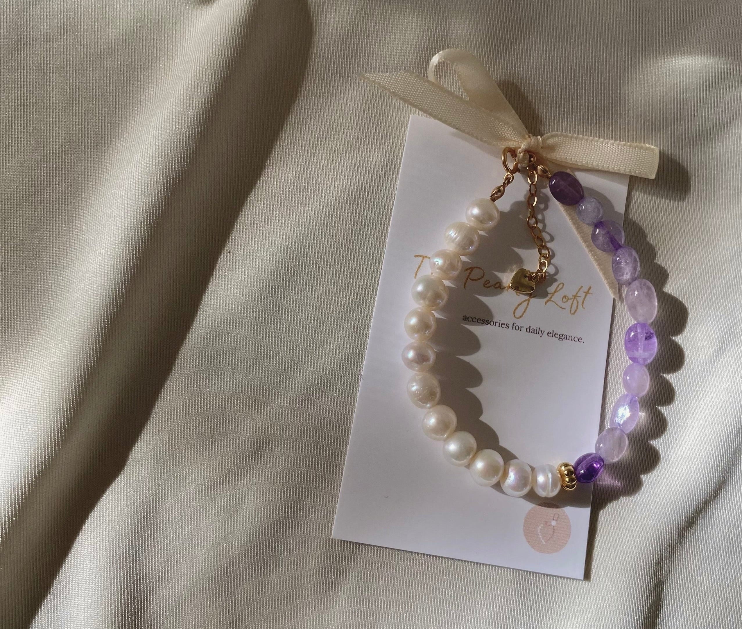 Beaded bracelet with pearls and amethyst on a white card, placed on a textured beige surface.