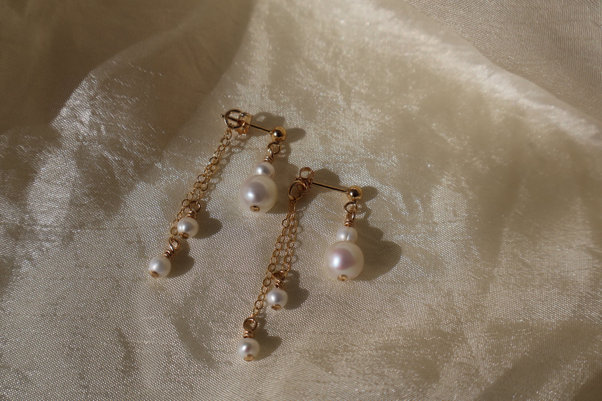 Pearl earrings with gold chains on a textured beige fabric background