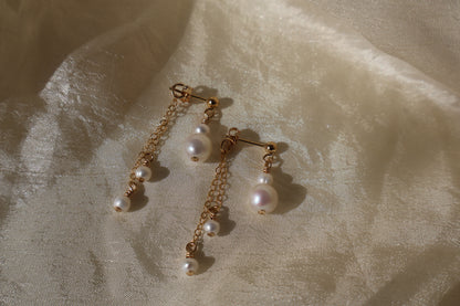 Pearl earrings with gold chains on a textured beige fabric background