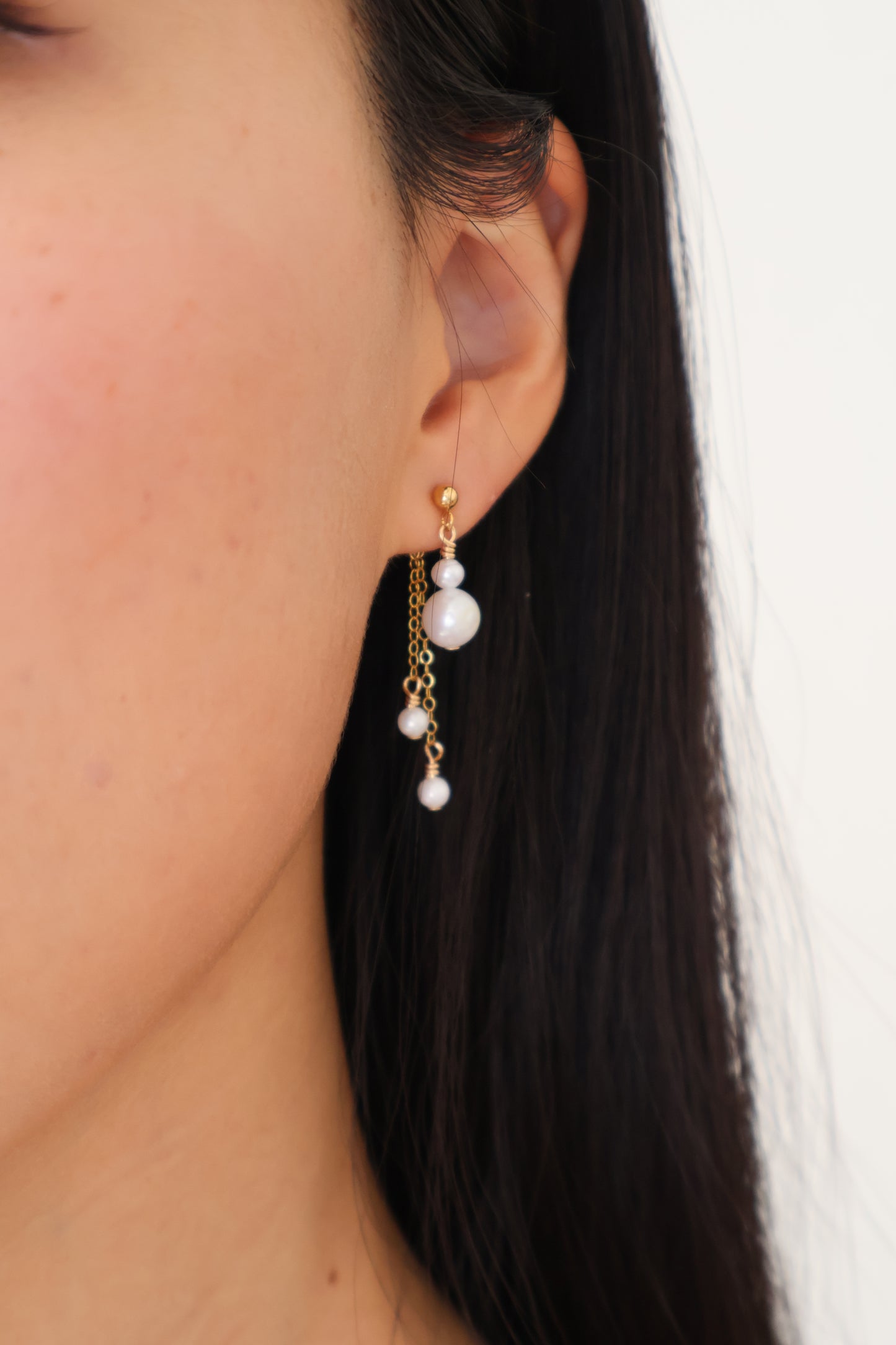 Close-up of an ear with a pearl earring against a neutral background