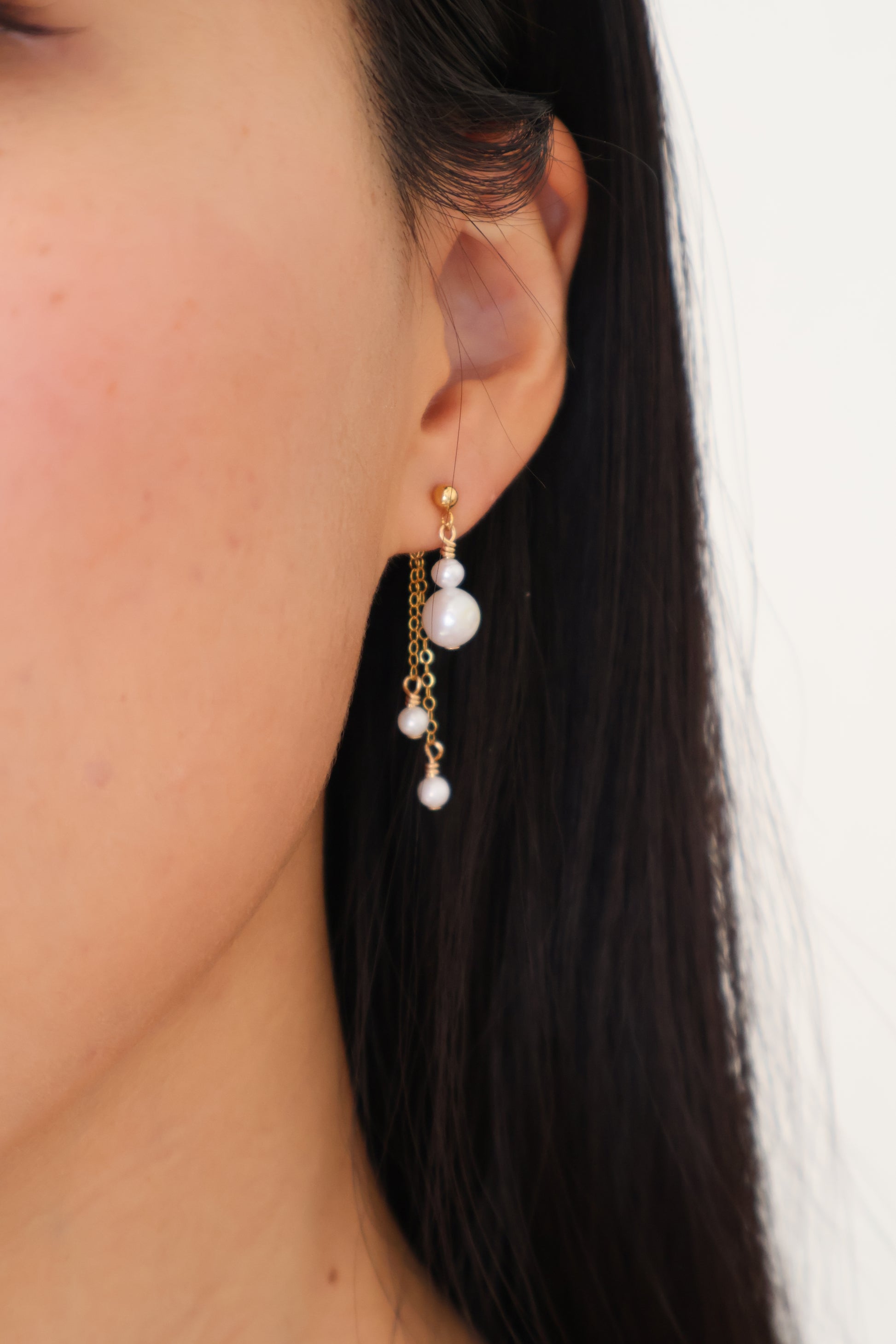 Close-up of an ear with a pearl earring against a neutral background