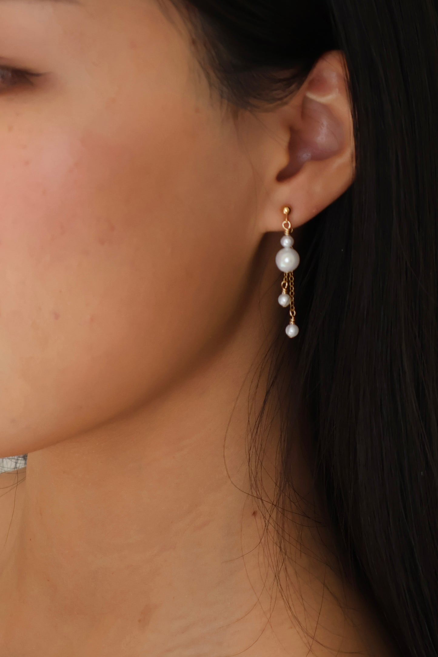 Close-up of a person wearing pearl earrings with a blurred background