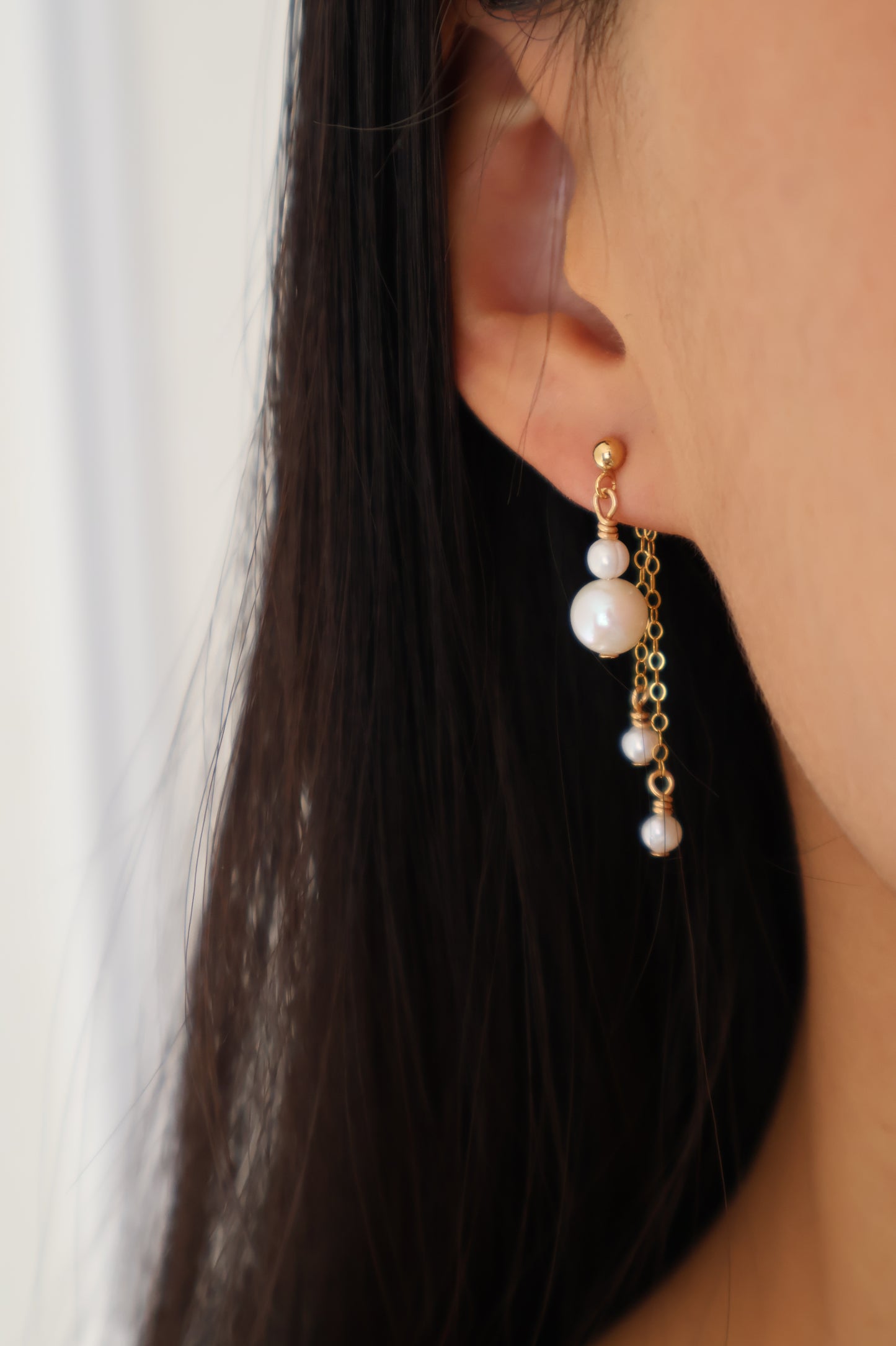 Close-up of an earring with pearls and gold chain on a person's ear.