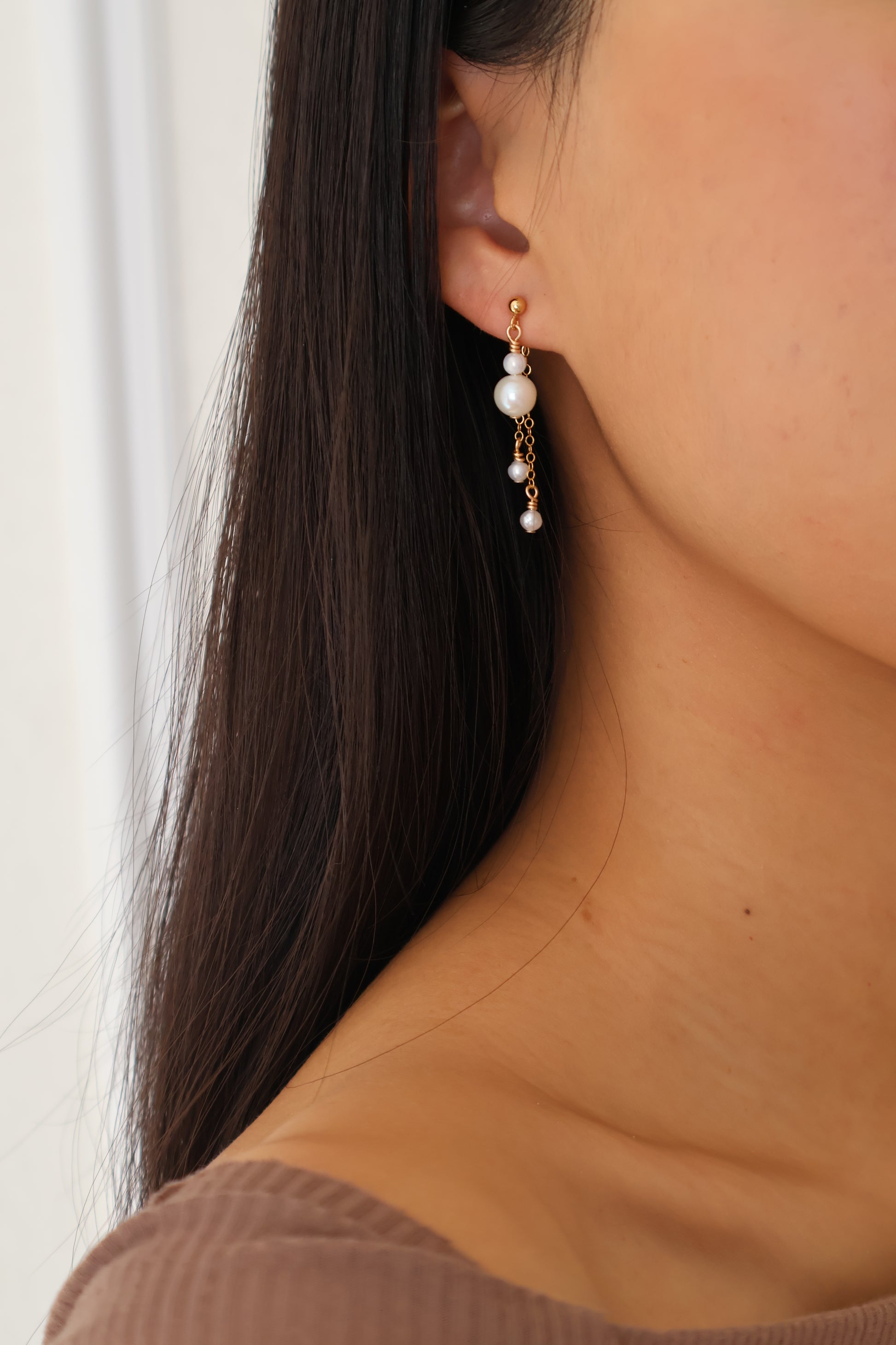 Close-up of an earring worn by a person with brown hair, wearing a brown jacket.