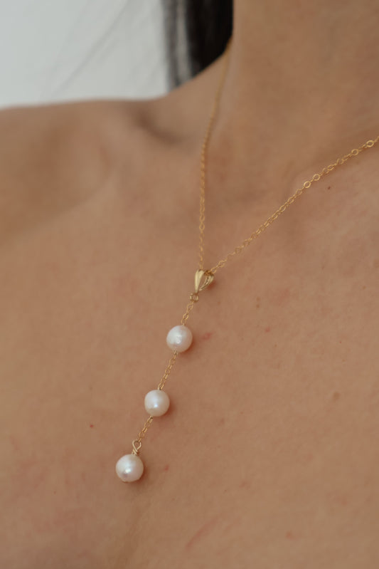 Gold lariat necklace with pearls draped on a neck