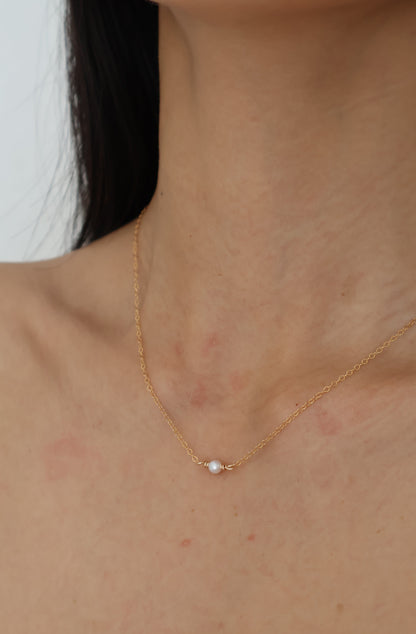 Gold necklace with a pearl pendant on a person's neck