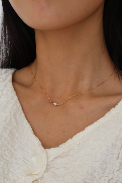 Close-up of a person wearing a delicate gold necklace with a pearl pendant.