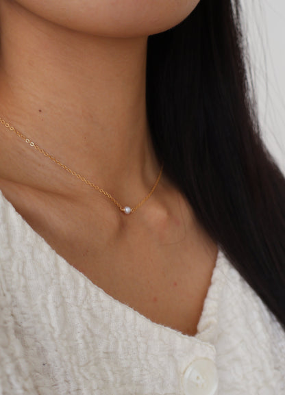 Close-up of a person wearing a delicate gold necklace with a small pendant.